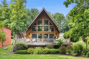 A large wooden cabin with a prominent gable roof, a covered porch, and a well-maintained garden. - Lodge style, 4 bedroom home on Lamoka Lake (Bradford)