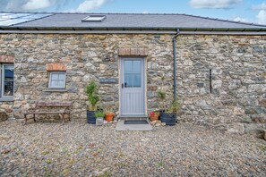 A stone cottage with a grey door, a bench, and potted plants. - Old Spot Cottage, Holiday Cottage Strumble Head Peninsula, Sleeps 6, 3 bedrooms,  bathrooms (Goodwick)