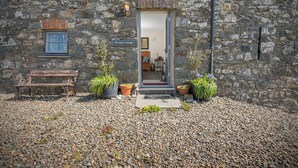 A stone cottage with a wooden bench, potted plants, and a sign reading 'Old Spot Cottage.'