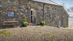 A stone cottage with a wooden bench, potted plants, and a sign reading 'Old Spot Cottage.'