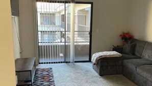 Un salon comprenant un canapé, un banc, un tapis à motifs, un ventilateur de plafond et une porte-fenêtre coulissante donnant sur l’extérieur.