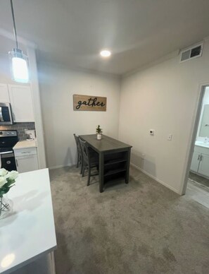 A compact kitchen with modern appliances, a dining area with a dark wooden table and chairs, and a 'gather' sign on the wall. - Downtown cozy and convenient (Phoenix)