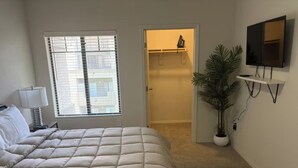Une chambre à coucher avec un lit, une fenêtre, une armoire, un téléviseur et une plante en pot.