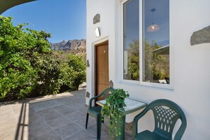 Eine Terrasse mit Tisch und Stühlen, eine Holztür und ein Fenster mit Blick auf eine gebirgige Landschaft.