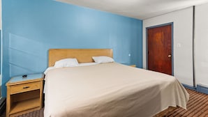 A hotel room with a bed, a nightstand, a wooden door, and a light fixture on the ceiling. - Budget INN (Flint)