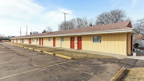 A row of motel rooms with individual doors and windows, a parking lot with visible cracks, and a grassy area in front. - Budget INN (Flint)