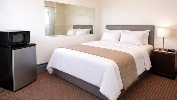 A hotel room with a bed, a small refrigerator, a bedside lamp, and a mirror on the wall. - Budget INN (Flint)