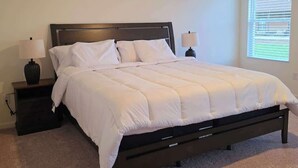 Un dormitorio con cama, dos mesitas de noche, una ventana con persianas y piso alfombrado.