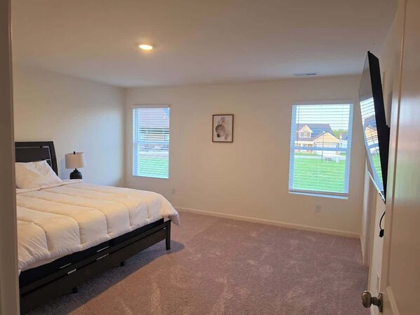 A bedroom with a bed, two windows, a picture on the wall, and a TV on the wall.