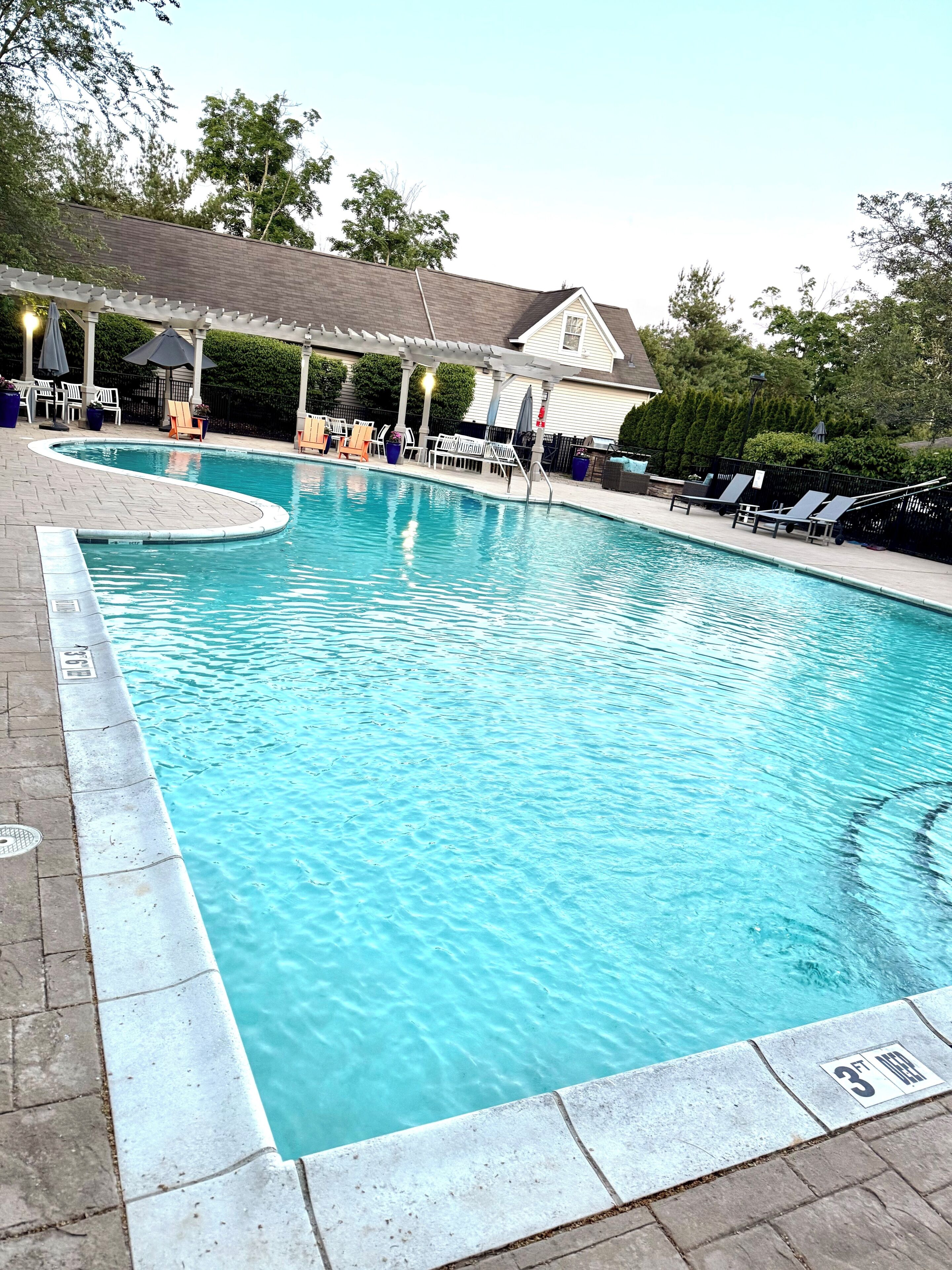 A rectangular swimming pool with a curved edge, surrounded by lounge chairs and a covered seating area.