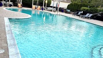 A rectangular swimming pool with a curved edge, surrounded by lounge chairs and a covered seating area.