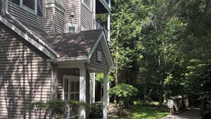 Ein zweistöckiges Haus mit einer überdachten Veranda, einem Weg zum Eingang und einem kleinen Garten mit Bäumen und Sträuchern.