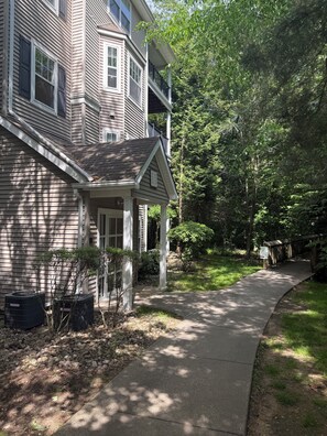 A two-story house with a covered porch, a pathway leading to the front door, and a small garden area with trees and shrubs.