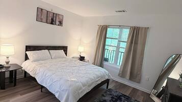 A bedroom with a bed, two bedside tables with lamps, a window with curtains, and a mirror.