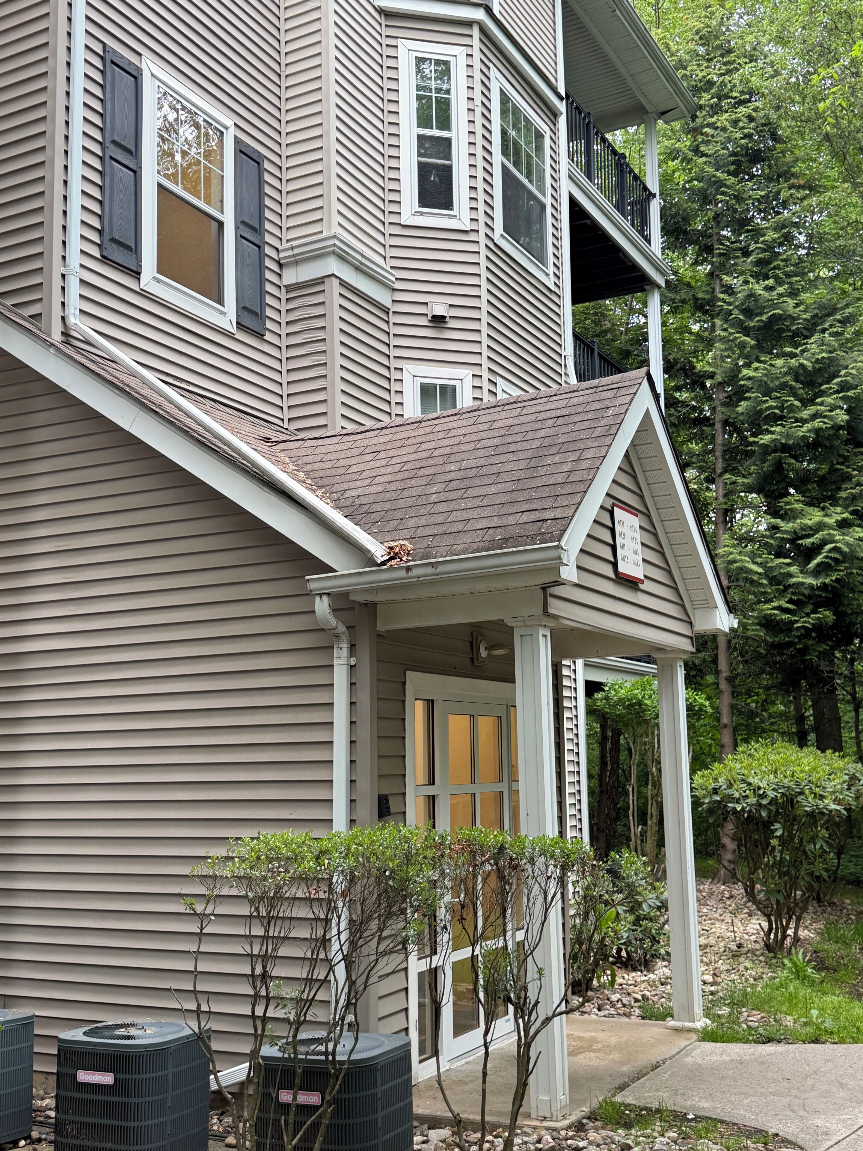 A multi-story building with a covered front porch, a visible air conditioning unit, and a small garden area.