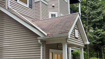 A multi-story building with a covered front porch, a visible air conditioning unit, and a small garden area.