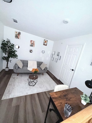 Una sala de estar con un sofá gris, una mesa de centro con flores, una planta en maceta y decoración en la pared.