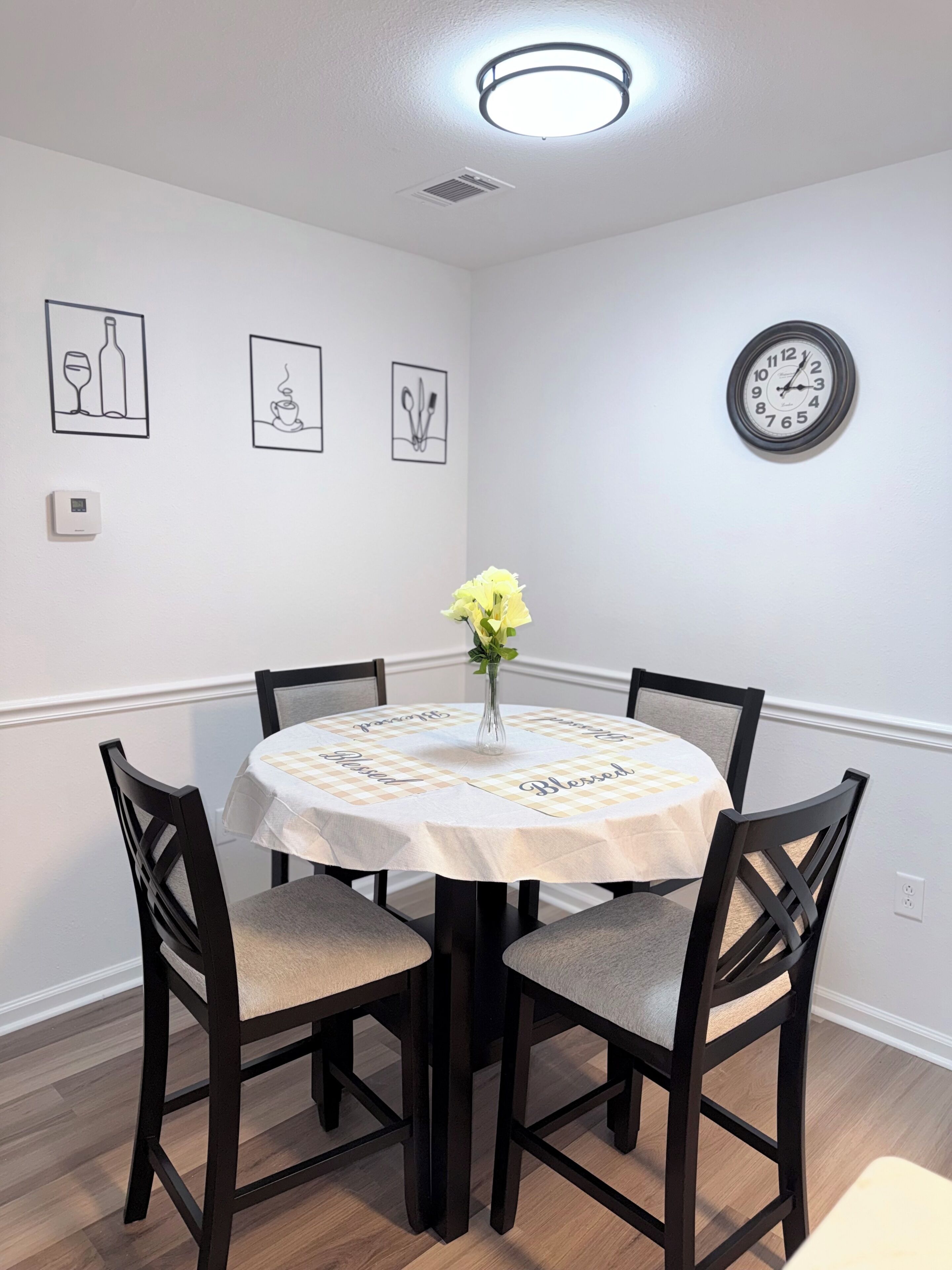 A dining area with a round table, four chairs, a vase with flowers, and wall art.