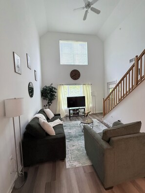 A living room with a sofa, a coffee table, a TV, a plant, and a staircase.