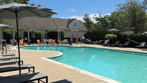 Ein Pool mit Liegestühlen und Sonnenschirmen, eine überdachte Terrasse und ein Haus im Hintergrund.