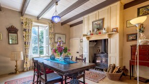 Un comedor con una mesa de madera, sillas, un jarrón con flores, un tapete estampado y una chimenea.