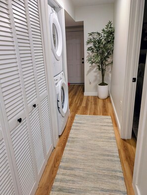 A laundry area with a washing machine and dryer, a wooden floor, a rug, and a potted plant.