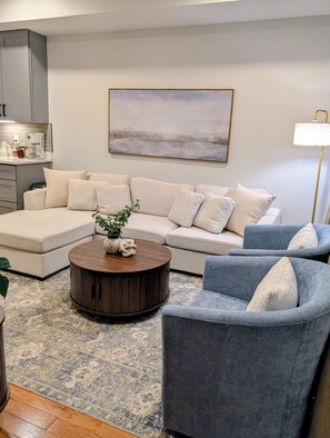 Un salon avec un canapé, un fauteuil, une table basse et un tableau accroché au mur.