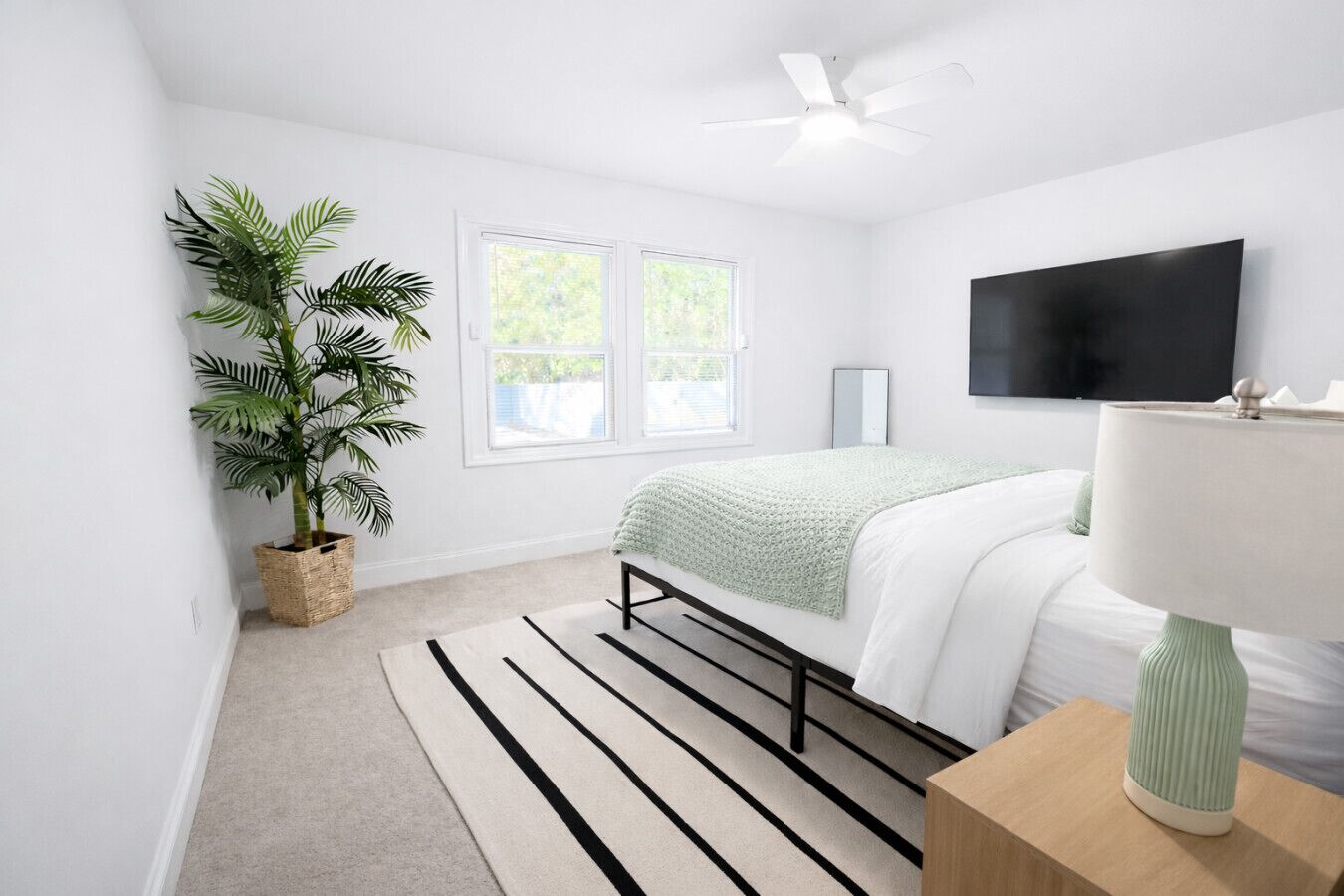 Un dormitorio con una cama, una planta en maceta, un televisor y un ventilador de techo.