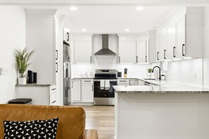Une cuisine moderne avec des meubles blancs, des appareils en acier inoxydable et un plan de travail en marbre.
