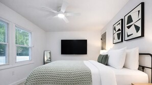 Ein Schlafzimmer mit Bett, Deckenventilator, Fernseher und Wandbild.