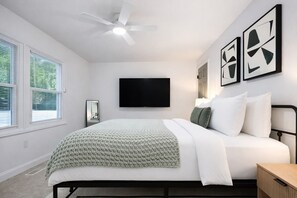 A bedroom with a bed, a ceiling fan, a TV, and artwork on the wall. - The Hidden Gem in North Myrtle Beach (North Myrtle Beach)