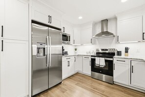 A modern kitchen with white cabinetry, stainless steel appliances, and a wooden floor. - The Hidden Gem in North Myrtle Beach (North Myrtle Beach)