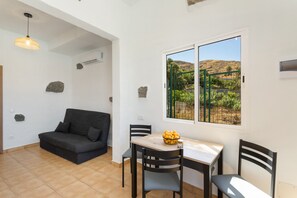 A room with a sofa, dining table, chairs, a window with a view of greenery, and a hanging light fixture. - Vacation Home 'Casa 3' with Mountain View, Wi-Fi and Air Conditioning (Taidía)