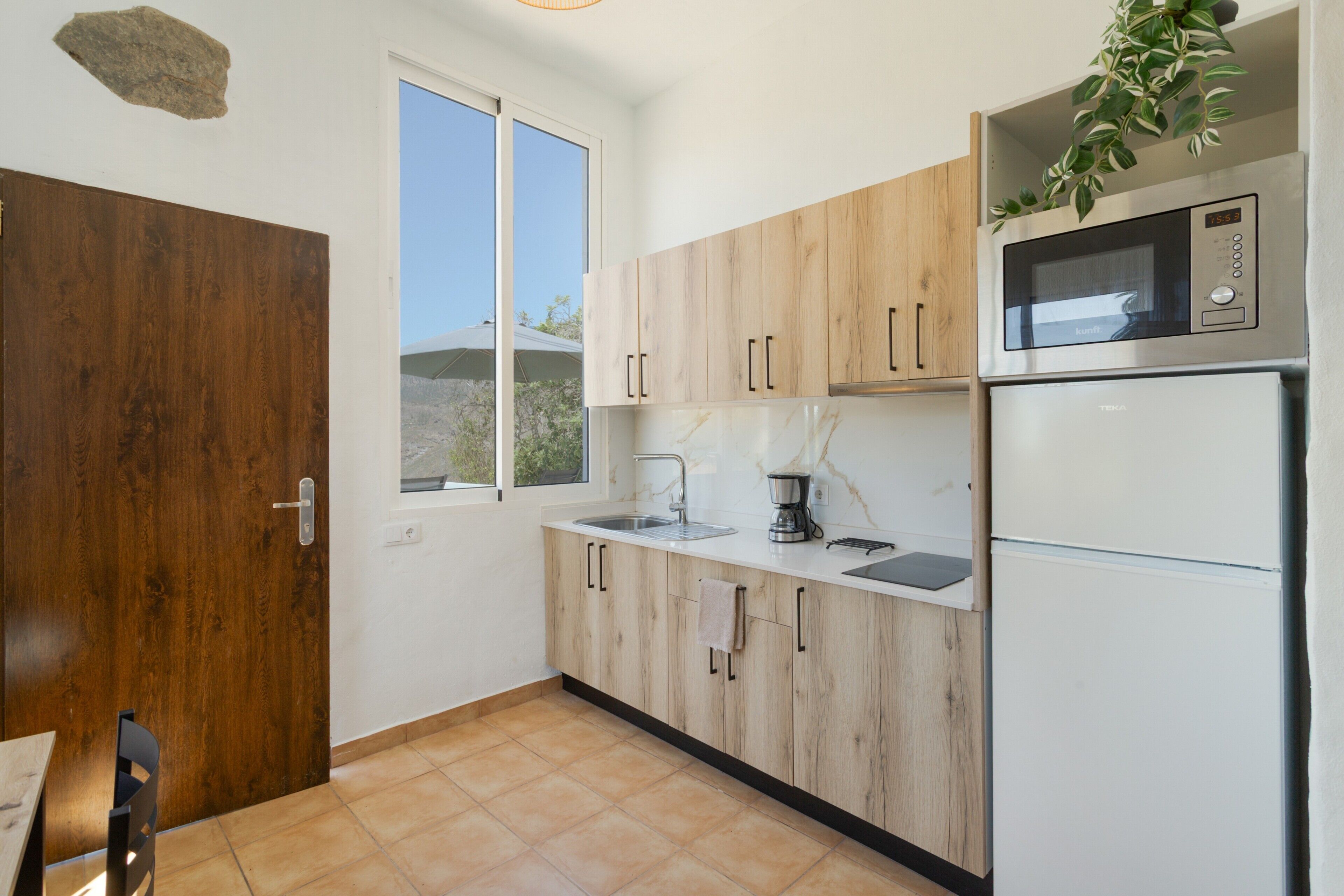 Una cocina con armarios de madera, microondas, fregadero y refrigerador.