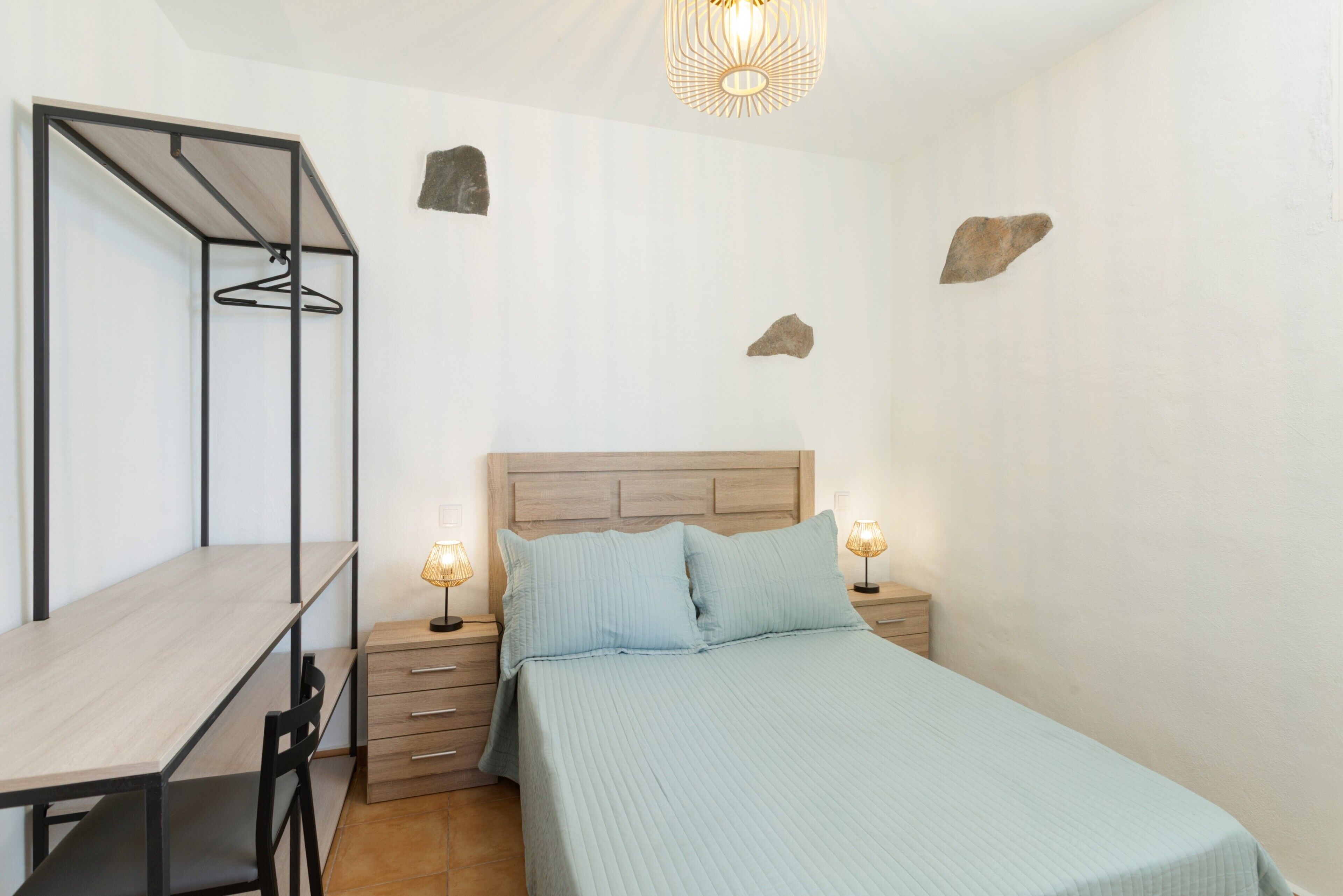 A bedroom with a bed, bedside tables, a desk, and a hanging wardrobe.