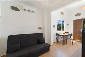 Une pièce avec un canapé noir, une table à manger avec des chaises, une fenêtre donnant sur un espace verdoyant et une porte.