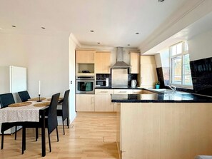 A modern kitchen with wooden cabinets, a central island, and a dining area with a table and chairs. - Islington Apartment by PrimeCityHosts (Greater London)