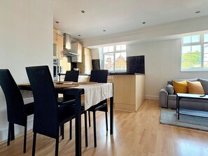 A modern kitchen with built-in appliances, a dining area with a table and chairs, a sofa, and large windows. - Islington Apartment by PrimeCityHosts (Greater London)