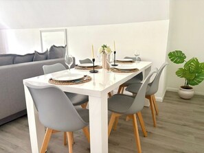 Ein Essbereich mit einem weißen Tisch, grauen Stühlen und einer grauen Couch im Hintergrund.