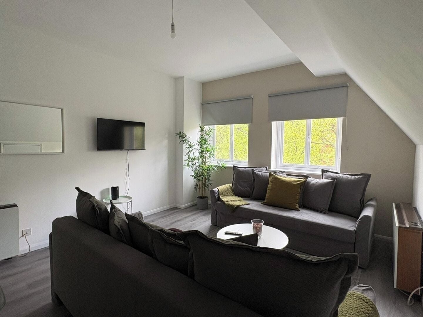 A modern living room with a sofa, a small table, a TV, and a window with blinds.