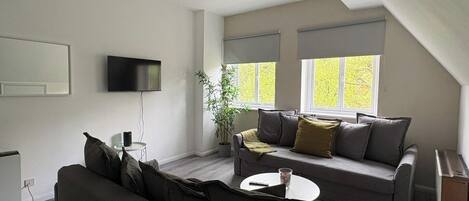 A modern living room with a sofa, a small table, a TV, and a window with blinds.