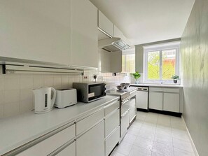 Eine moderne Küche mit weißen Schränken, einer Mikrowelle, einem Toaster und einem Fenster mit Blick ins Grüne.