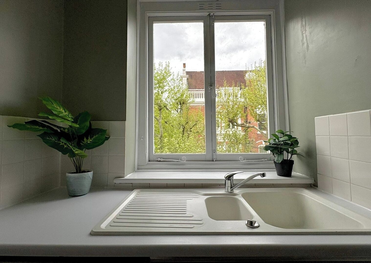 Eine Küche mit Fenster, Spüle und zwei Blumentöpfen.