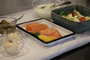 A table with a dish of salmon, a bowl of salad, and small containers of olives and cream.