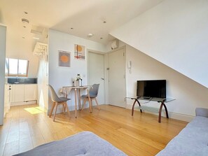 Ein modernes Wohnzimmer mit Essbereich, einem Fernseher auf einem Schrank und einer im Hintergrund sichtbaren Küche.