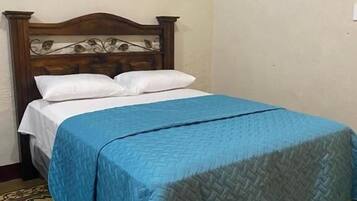 A single bed with a wooden headboard, white pillows, and a blue quilt. The floor has a patterned tile design.