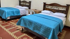 Two single beds with wooden headboards, a small table, and a chair in a room with patterned floor tiles. - Hotel Malybu (Guatemala City)