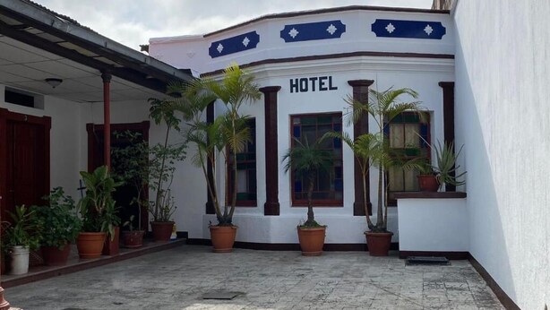 A hotel with a white facade, columns, and potted plants in the courtyard. - Hotel Malybu (Guatemala City)