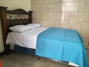Una cama con cabecera de madera, ropa de cama blanca y colcha azul.