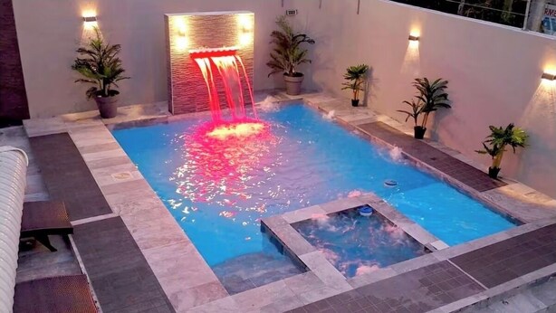 Ein Schwimmbecken mit Wasserspiel, umgeben von Fliesenböden und Kübelpflanzen.